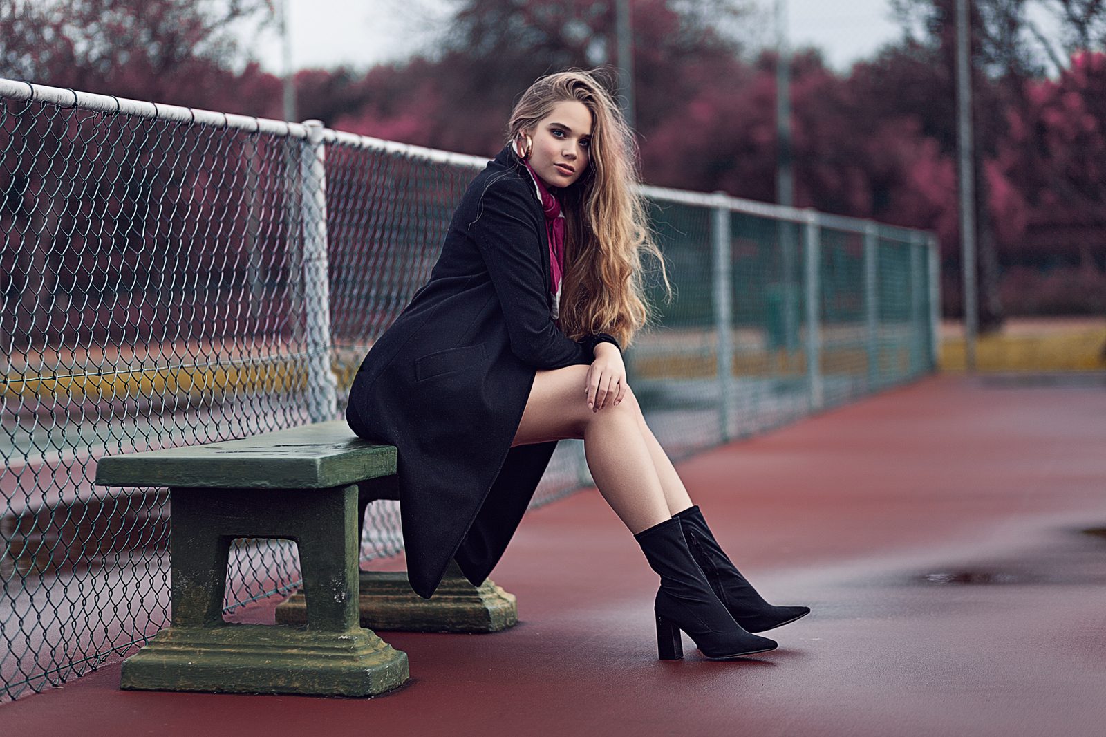 Seated portrait in a long coat beside a court fence