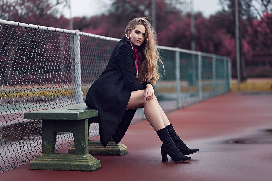 Seated portrait in a long coat beside a court fence