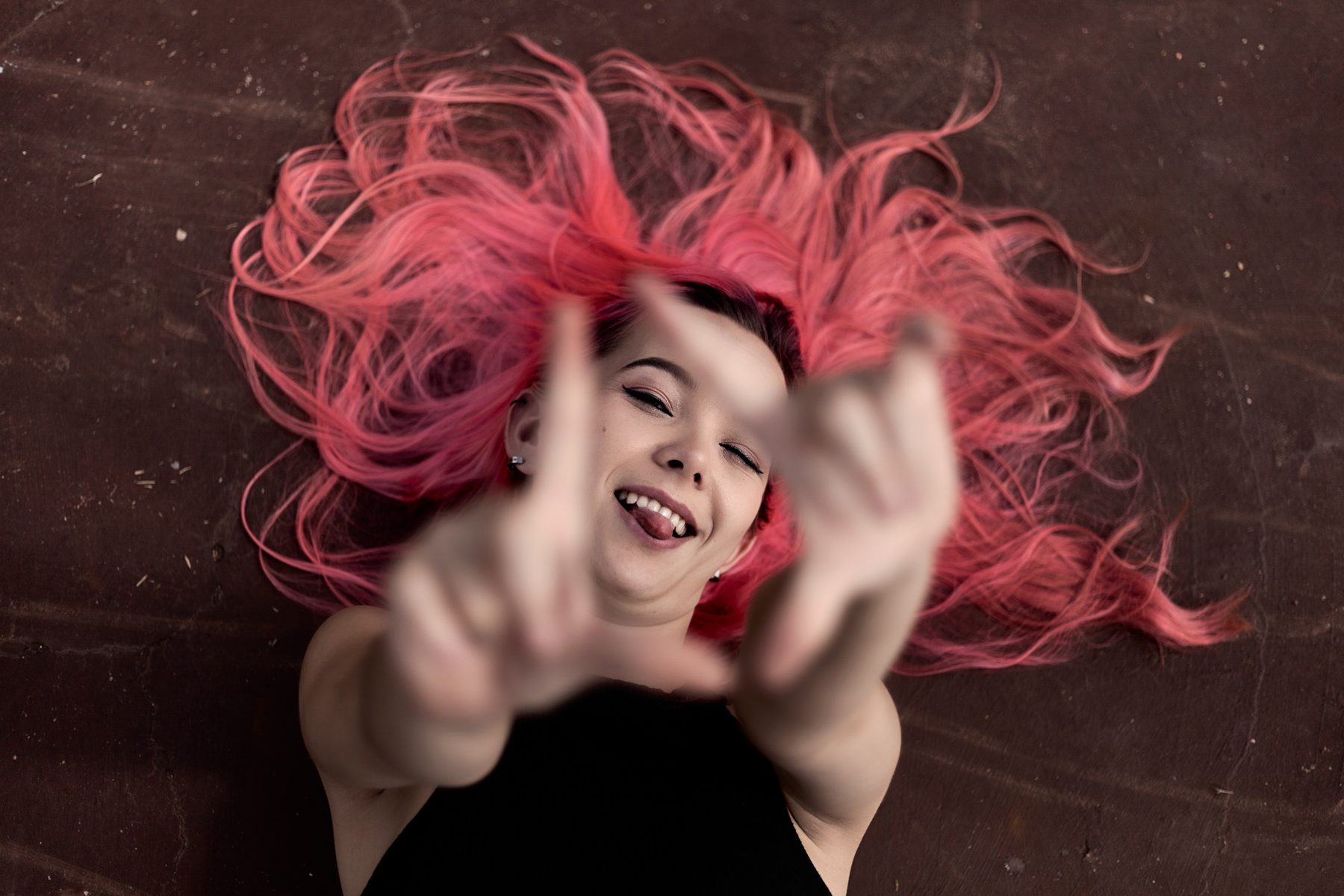 Portrait with pink hair fanned out across a dark floor